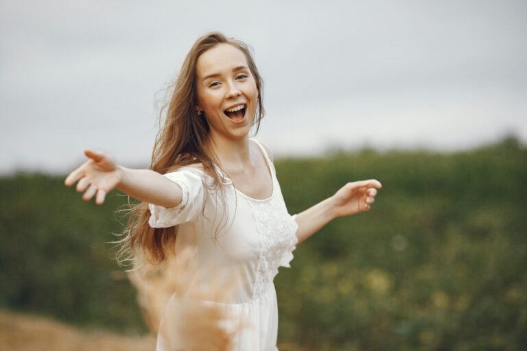 Smiling woman in a white dress enjoying nature with open arms.